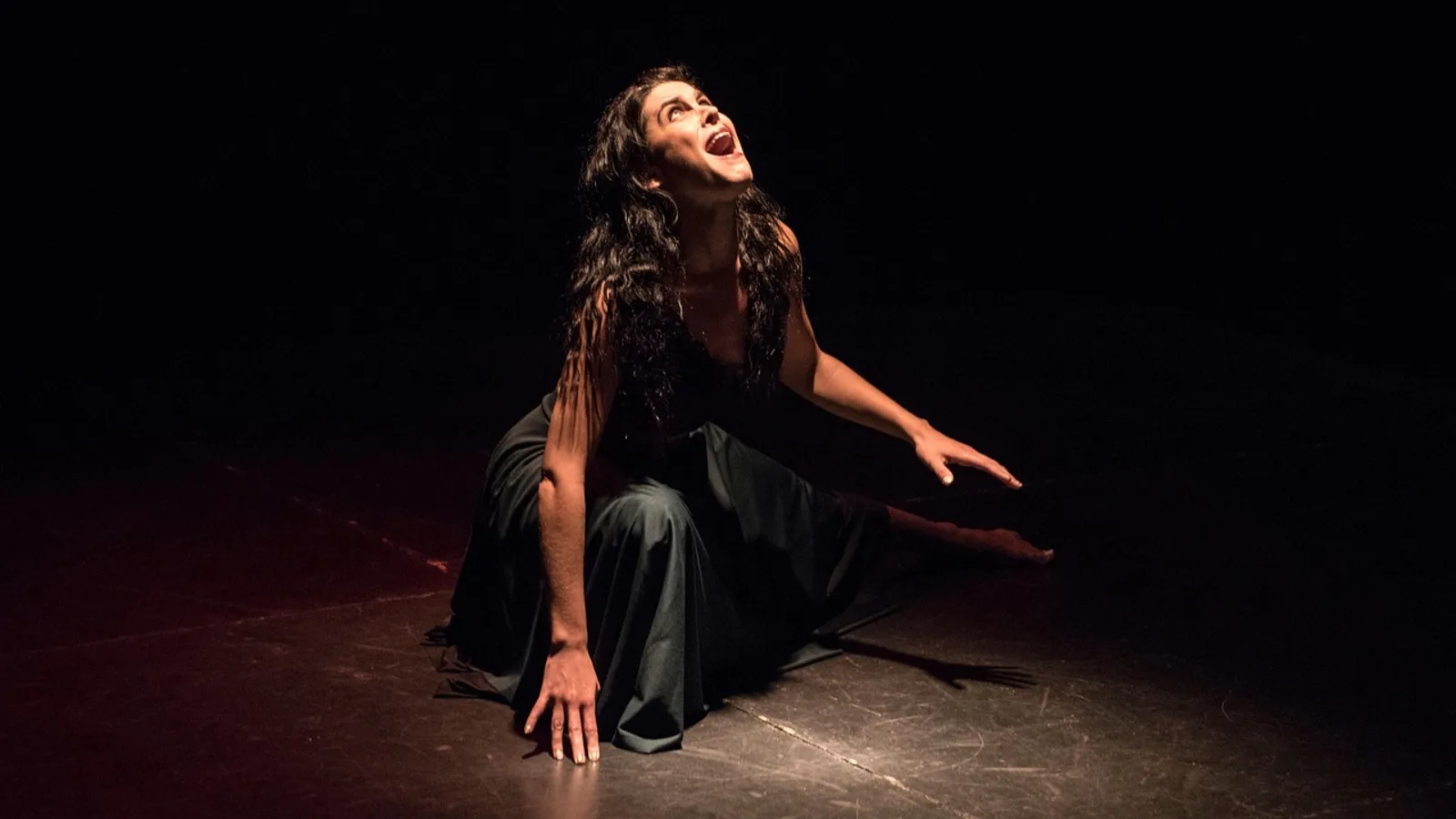 An actress delivering an intense performance on a dark stage under a spotlight.