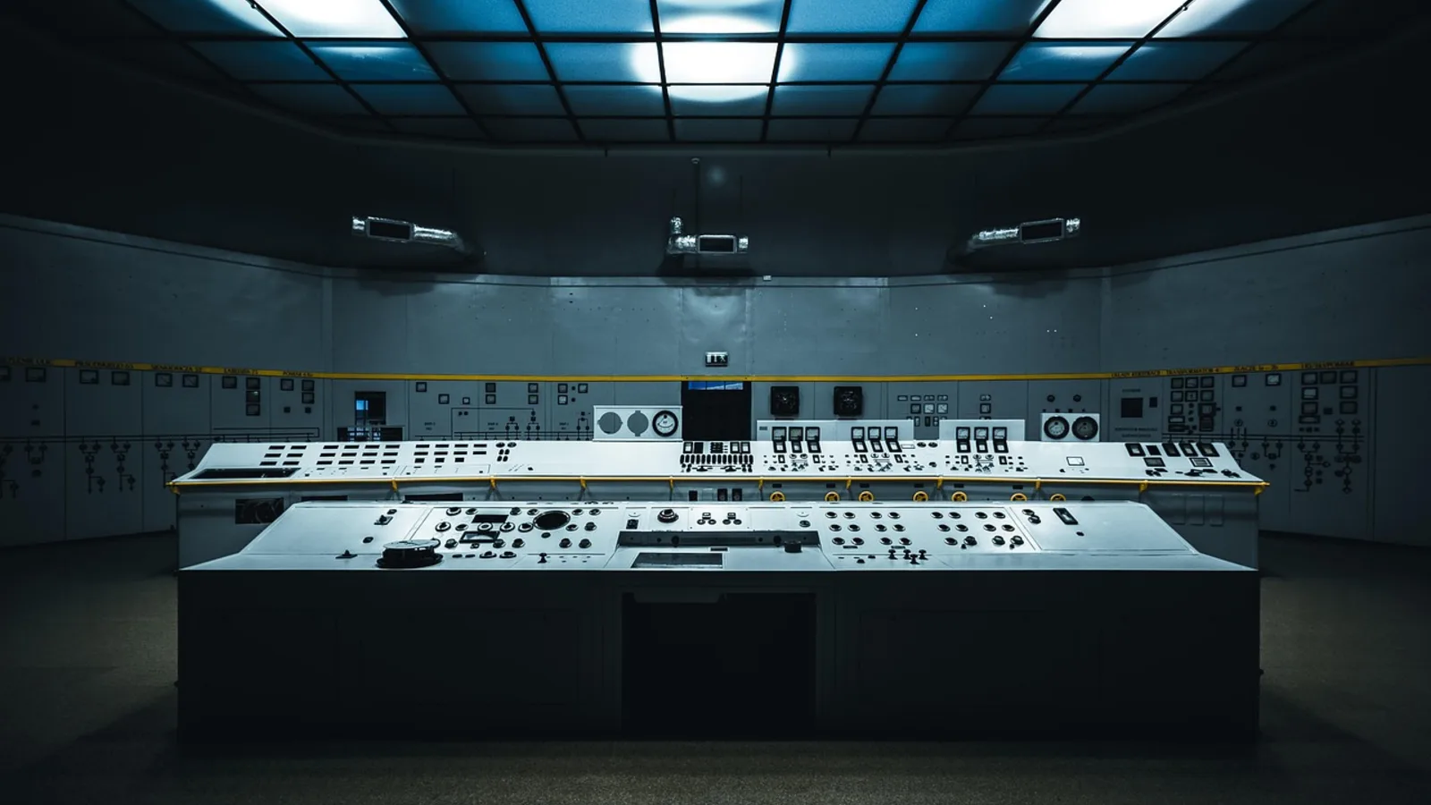 Dark control room with long consoles and an illuminated ceiling.